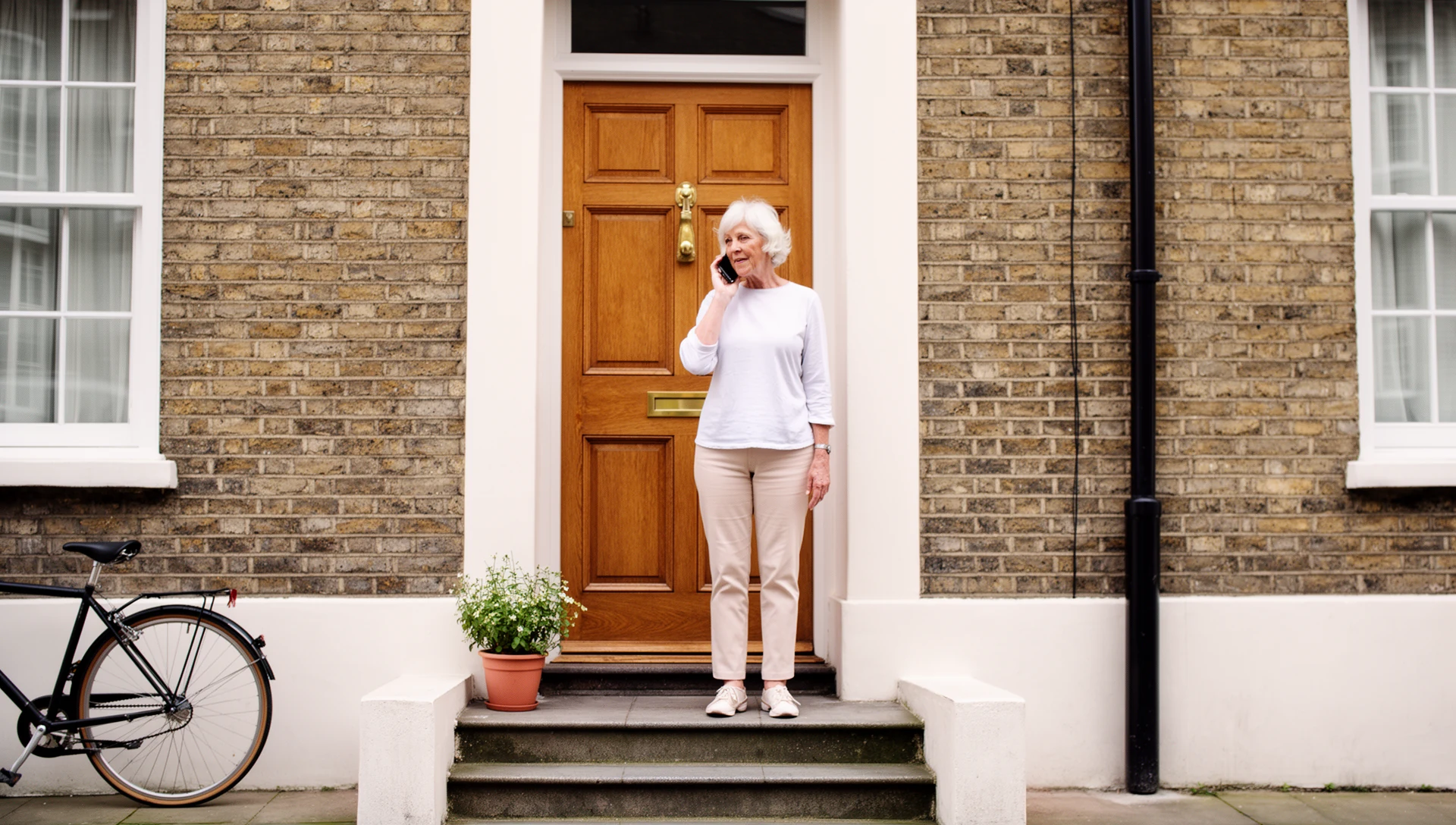 An older woman making a phone call as she arrives at the front door of her UK terraced house.
